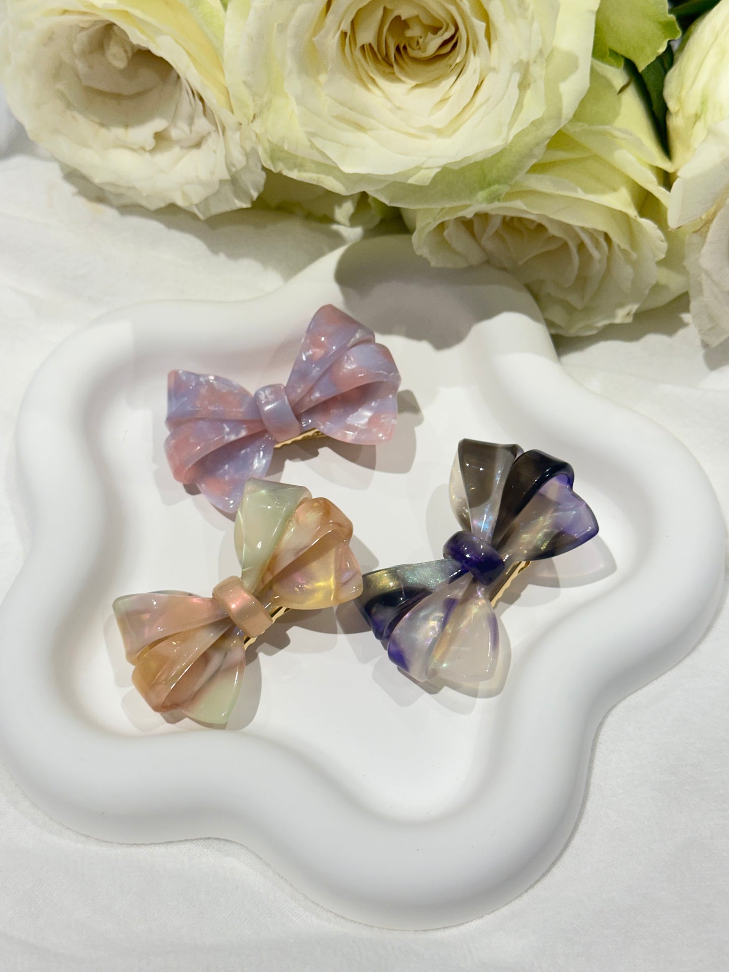 3 ombré aztec bow hair clip on a white heart-shaped stand with white roses in the background. only at petite murmure