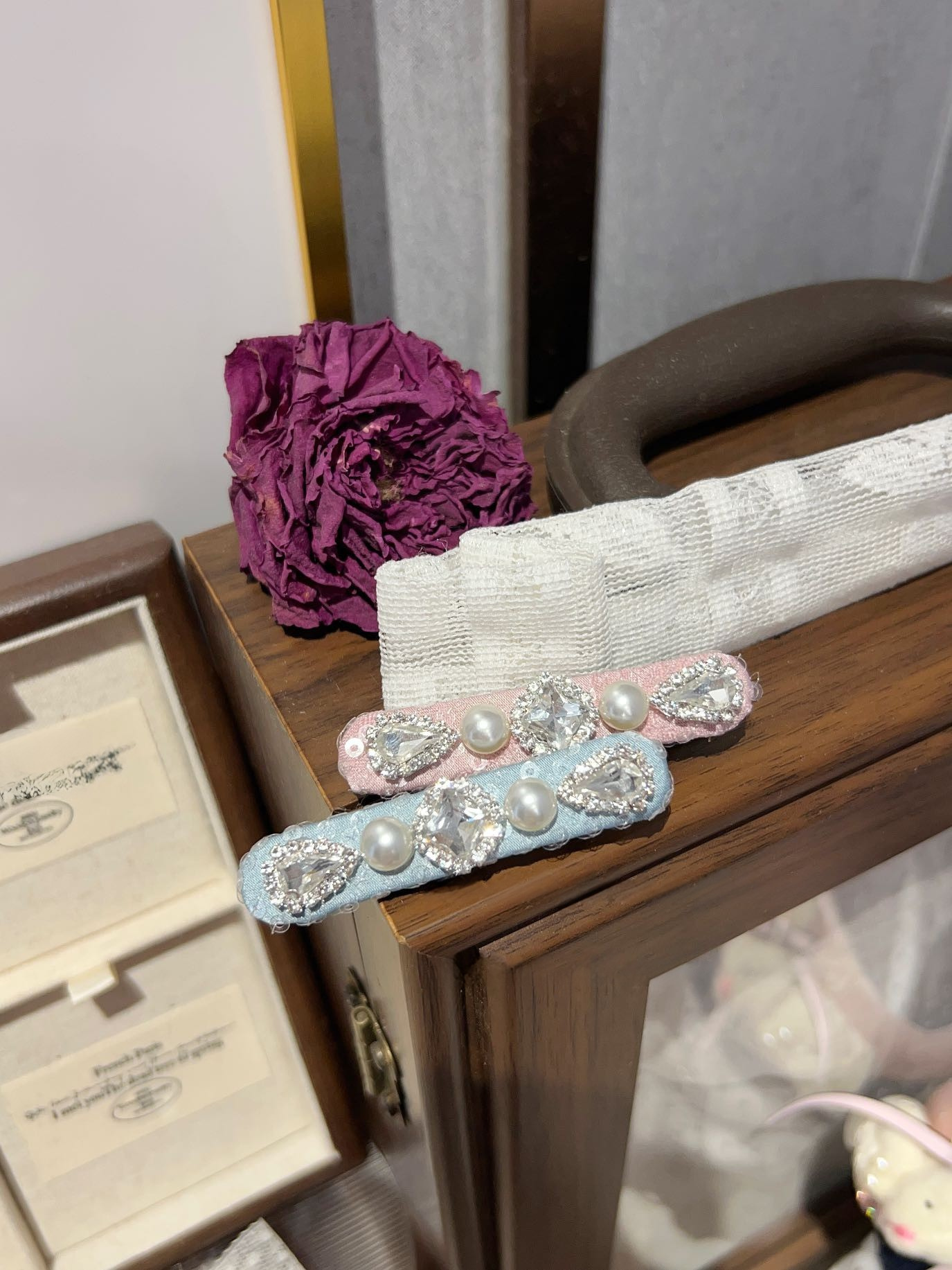 handmade decorative lace hair clip with pearls and Swarovski crystals on a soft neutral background on a wooden surface with a purple flower and jewelry box.Only at Petite Murmure