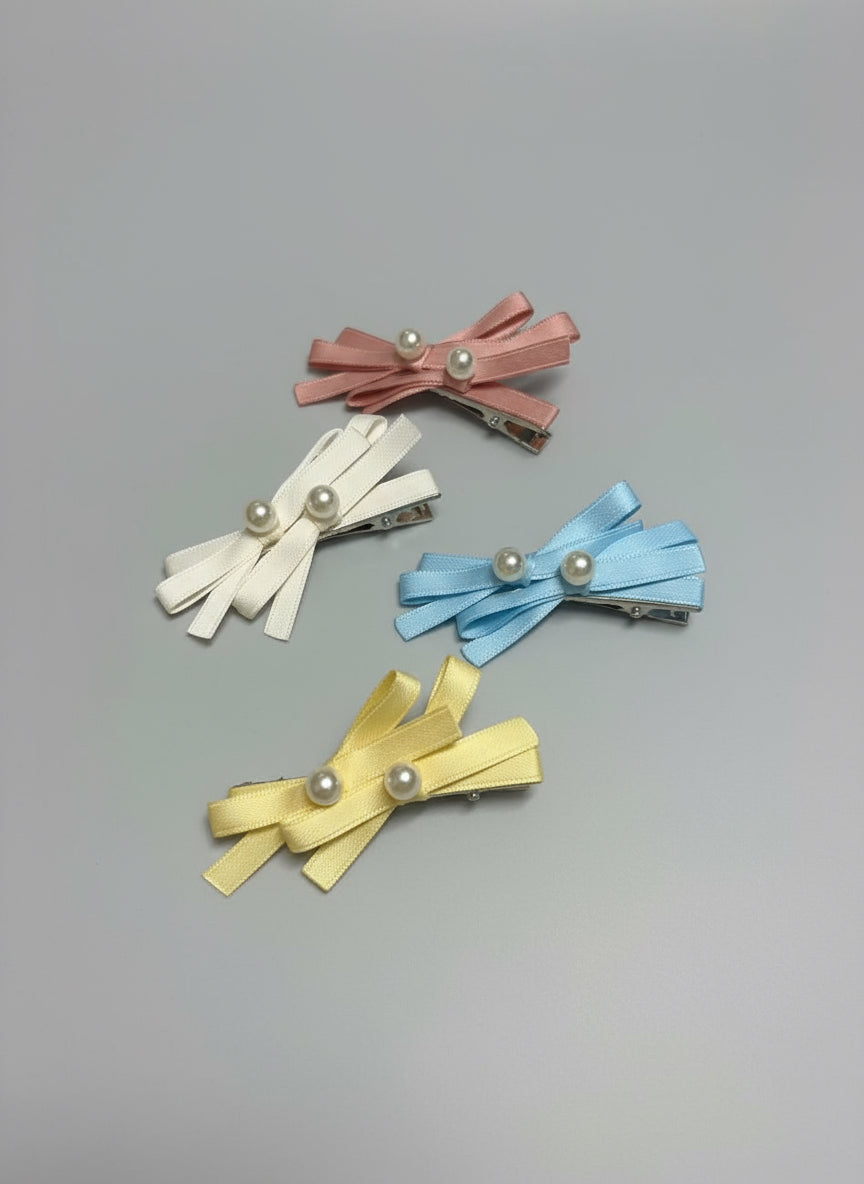 Set of four colorful hair clips with layered bows and pearl detailed designs on a gray background