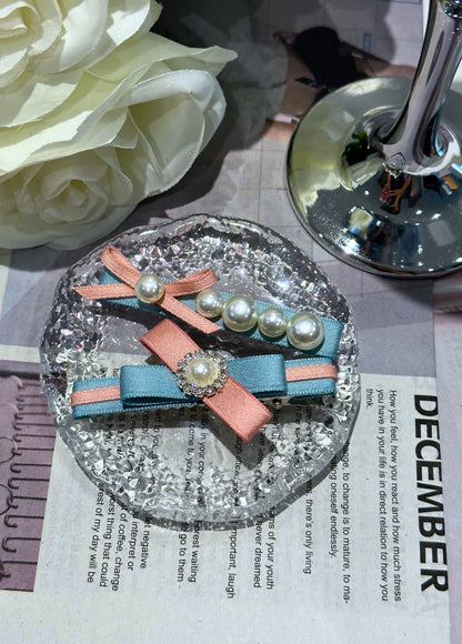 Set of pink and blue colorblock hair clips with ribbons and pearls on a textured surface.