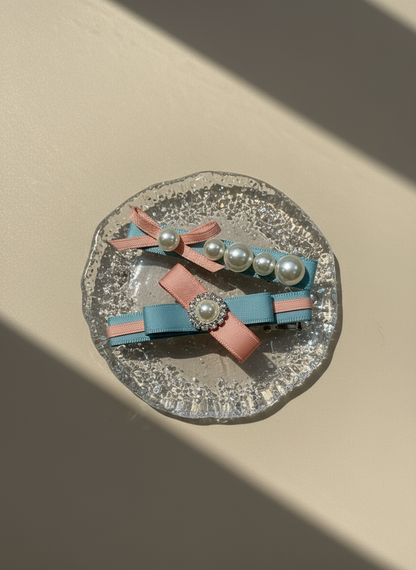 Pair of pink and blue colorblock hair clips with ribbons and pearls on a textured surface