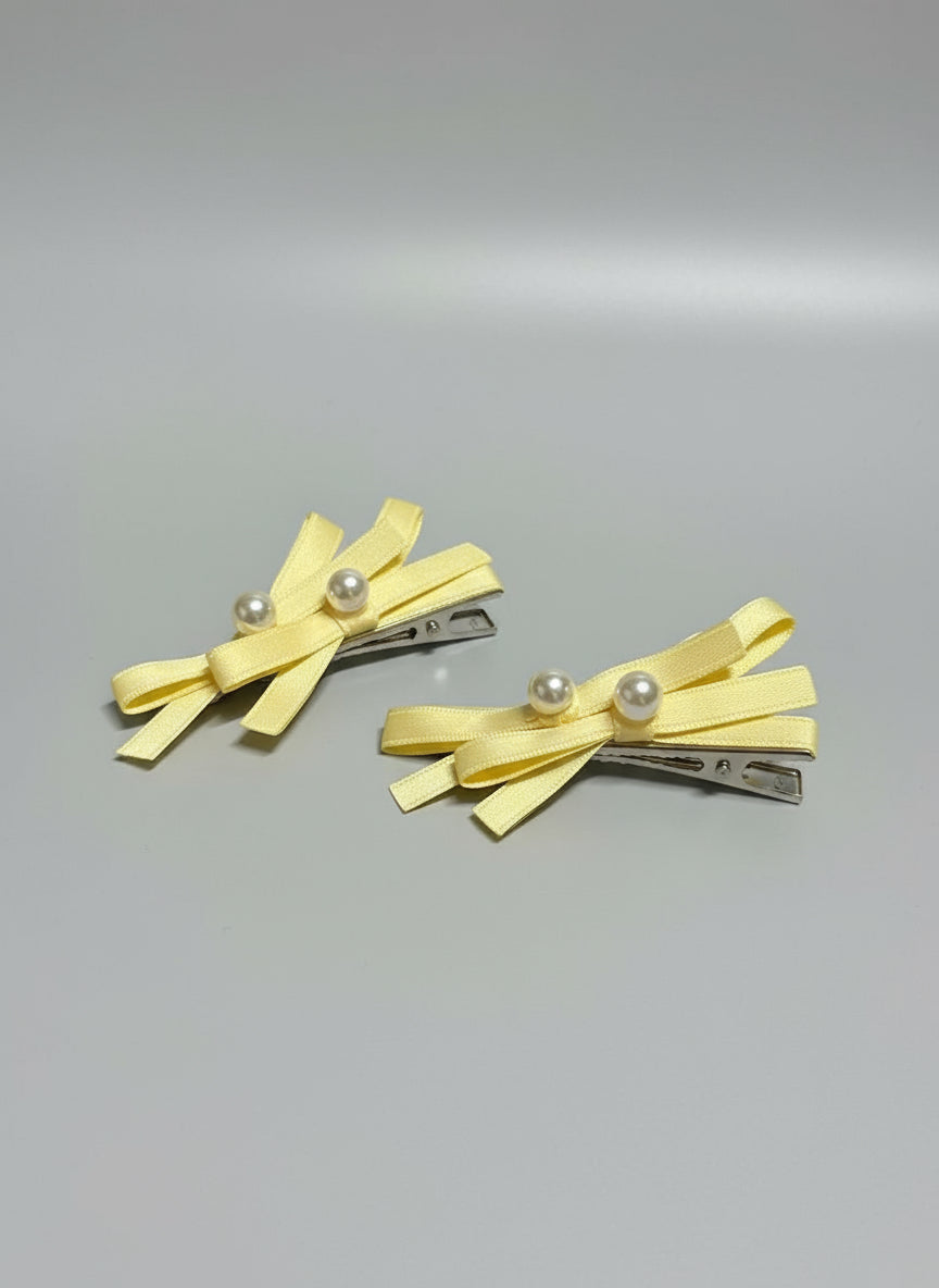 Two yellow hair clips with bow designs and pearl embellishments on a gray background