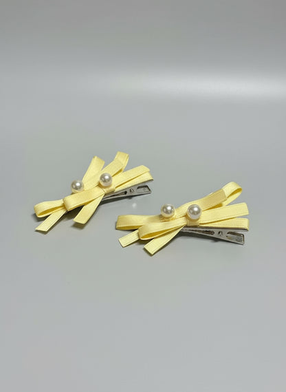 Two yellow hair clips with bow designs and pearl embellishments on a gray background
