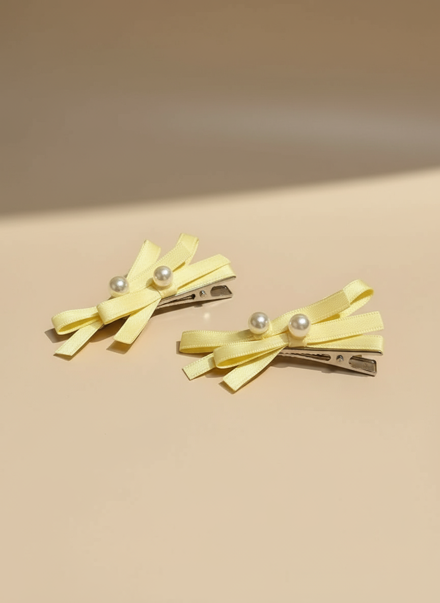 Two yellow hair clips with layered  bows pearl accents on a beige background