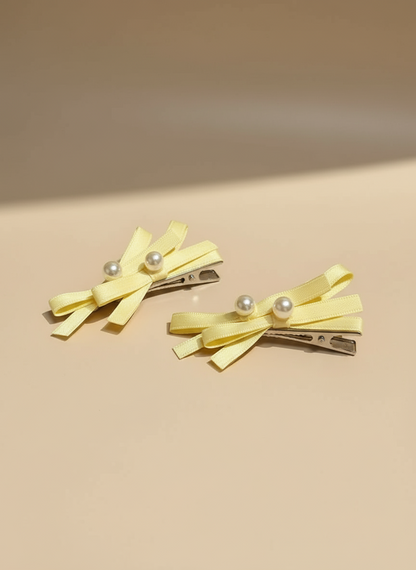 Two yellow hair clips with layered  bows pearl accents on a beige background
