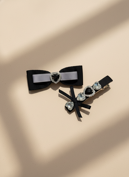 Two decorative black hair bows with heart-shaped Swarovski crystal centers hair clips/accessories on a beige background
