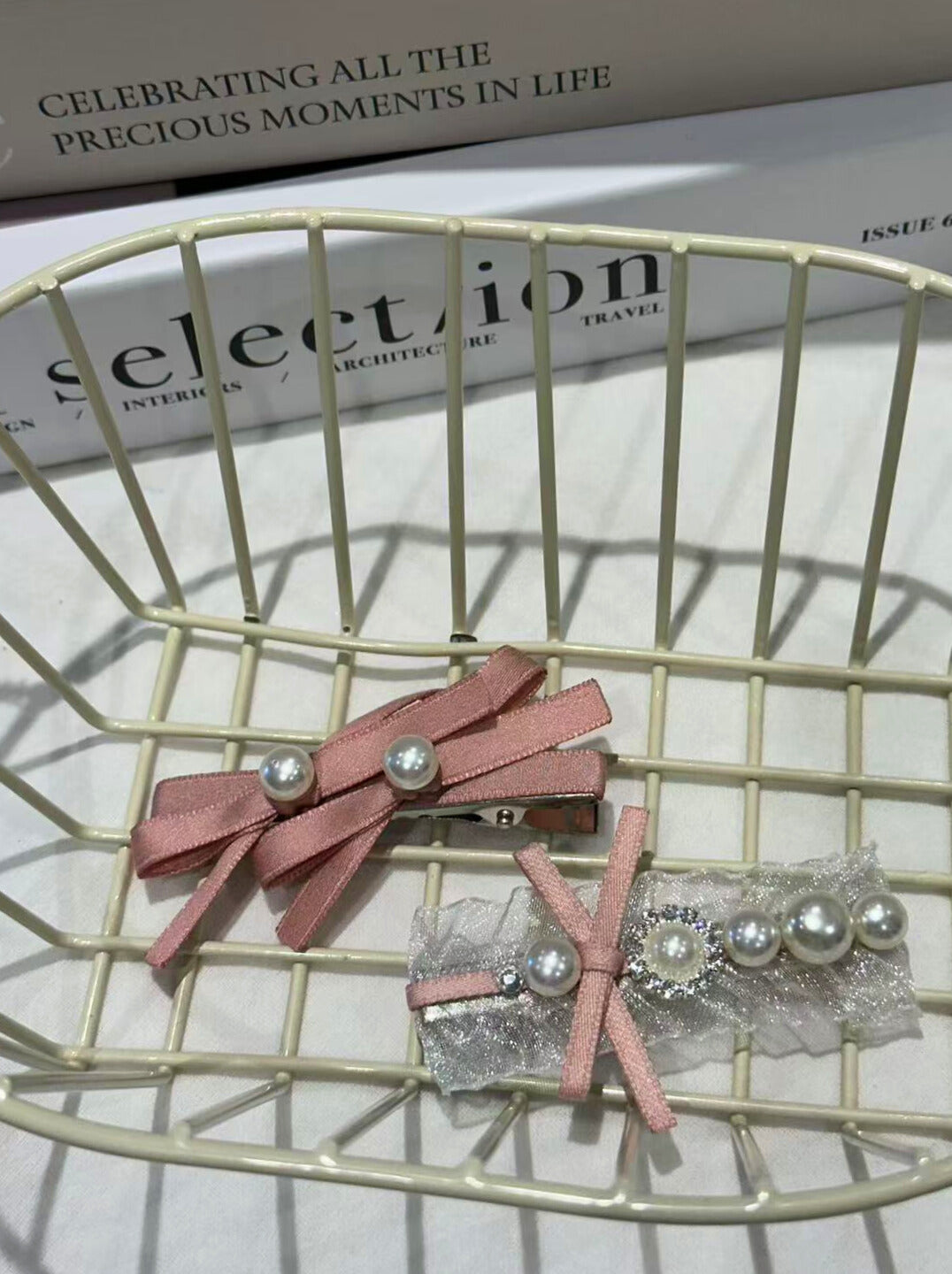 Pink hair clips with pearl accents on a wire basket, with 'selection' magazine in the background.