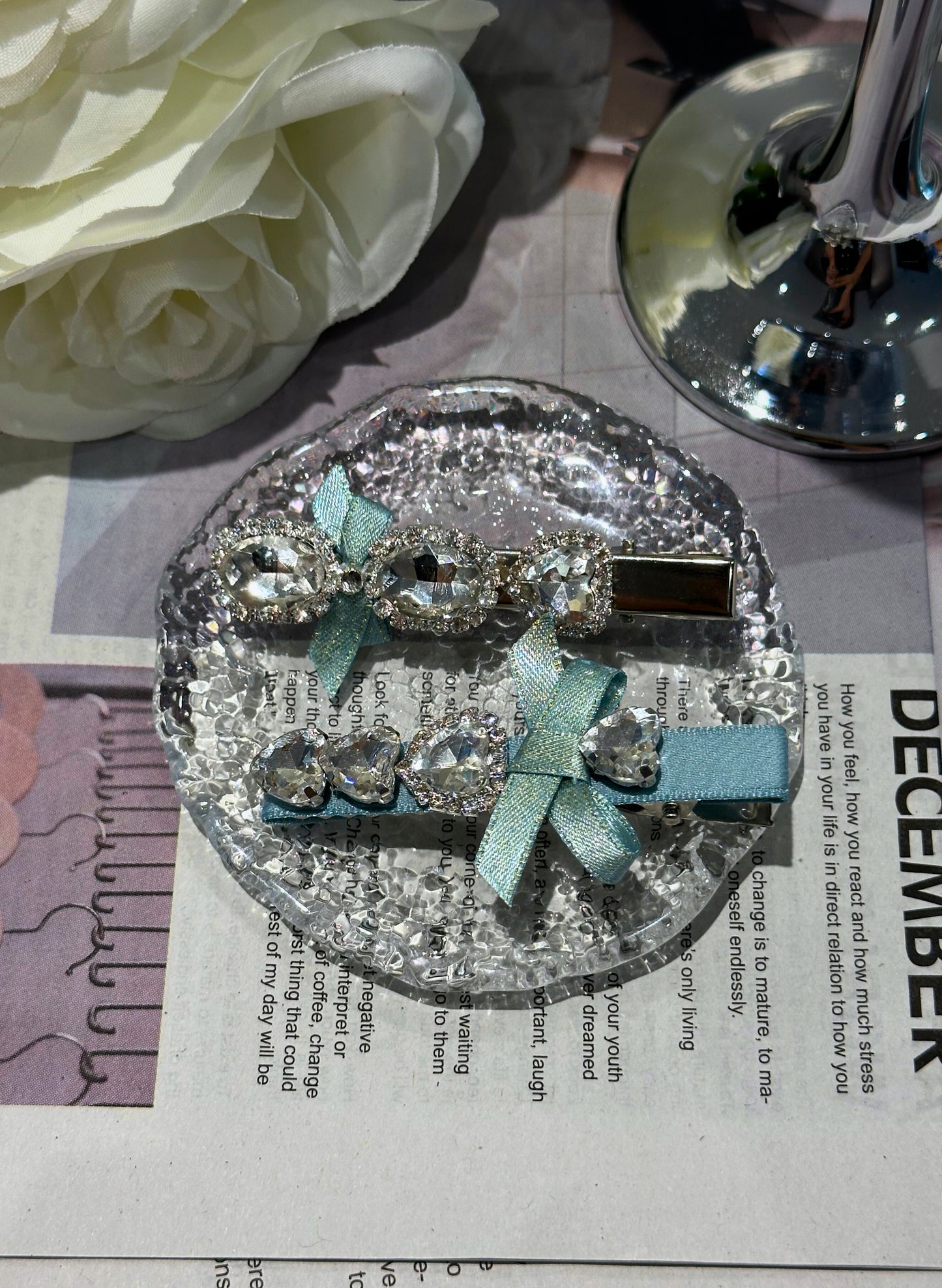 Decorative hair clip with Swarovski crystals and blue ribbons on a newspaper background