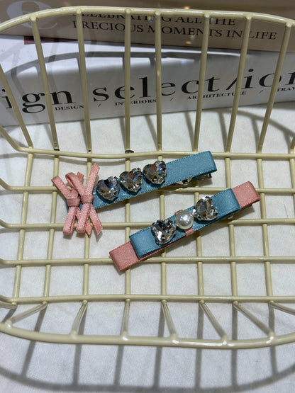 Two decorative hair clips with pink and blue ribbons and pearl and Swarovski crystals on a wire basket.