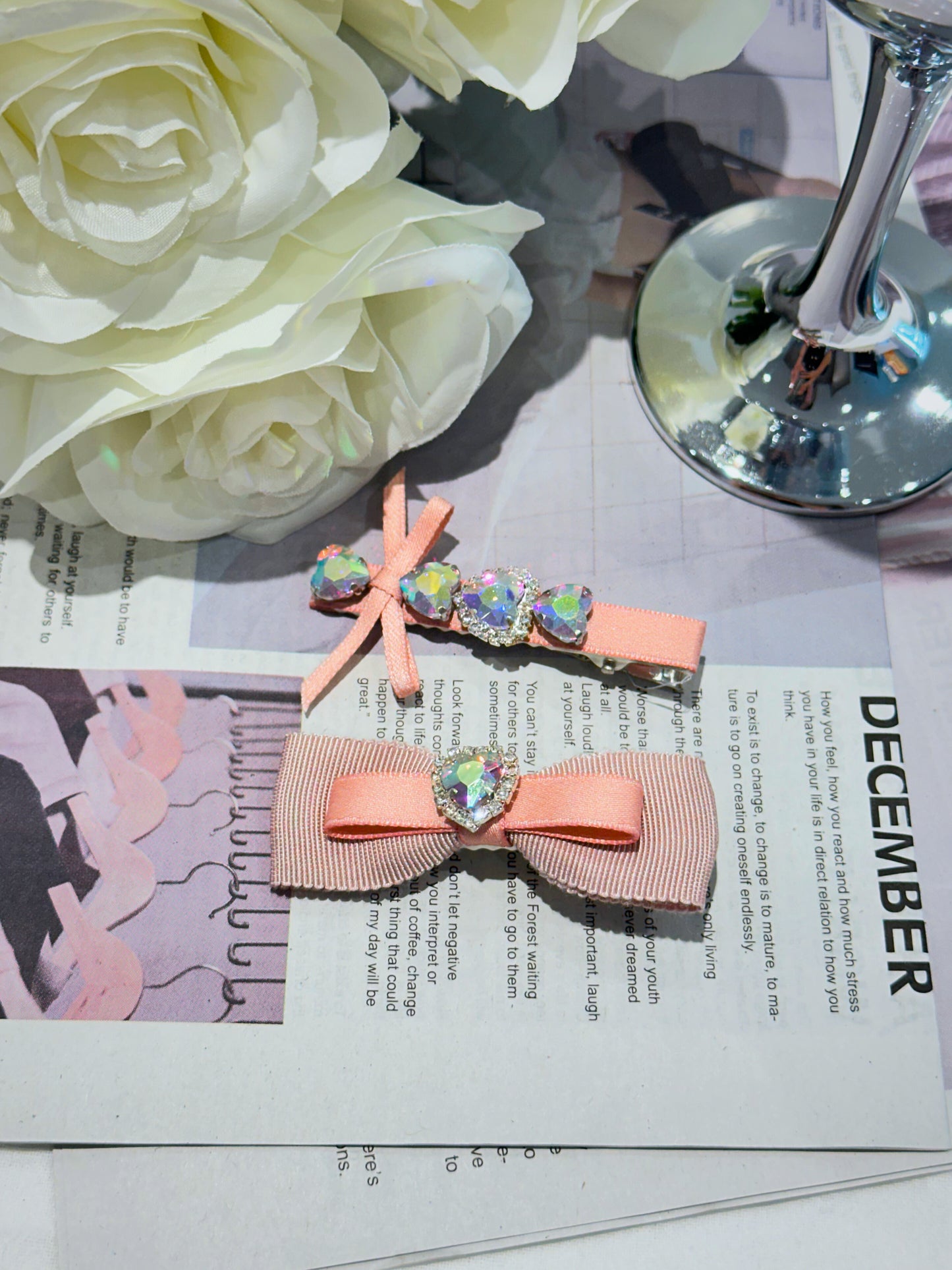 Two pink hair bows with heart-shaped Swarovski crystal centered hair clips with decorative elements on a magazine page with flowers in the background