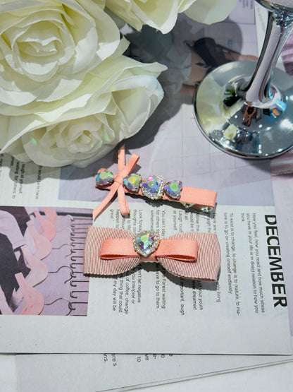 Two pink hair bows with heart-shaped Swarovski crystal centered hair clips with decorative elements on a magazine page with flowers in the background