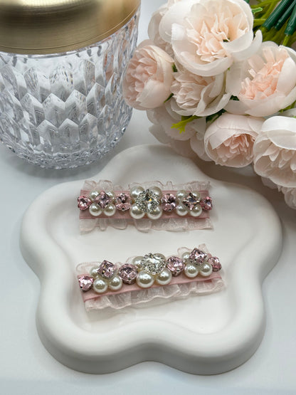Pair of hair clips with Swarovski crystals and pearls embellished and silky organza on white star-shaped plate, surrounded by flowers and a crystal vase. Only at petite murmure
