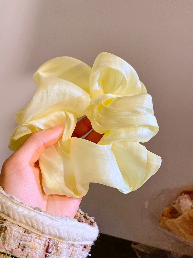 Hand holding a light yellow scrunchie against a neutral background
