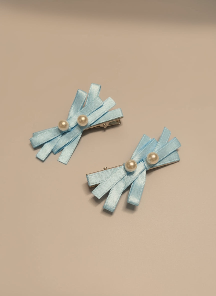 Pair of light blue hair bows with pearl centered hair clips on a beige background