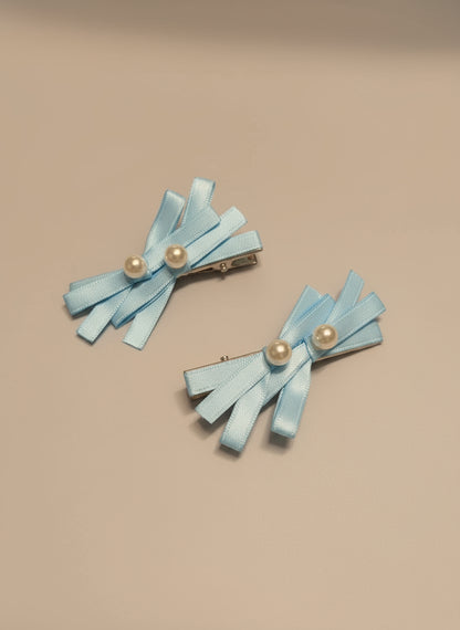 Pair of light blue hair bows with pearl centered hair clips on a beige background