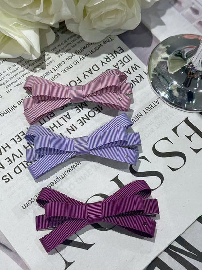 Three hair bows in pink, purple, and red on a newspaper background