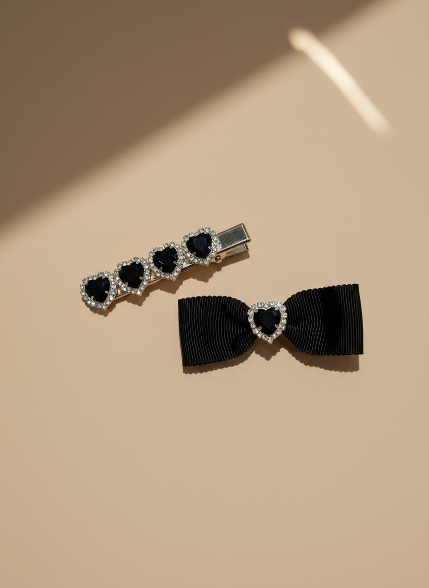 Set of hair accessories including a hair clip with black ribbons and heart shaped Swarovski crystals.  Black hair bow with heart-shaped gemstones on a beige background