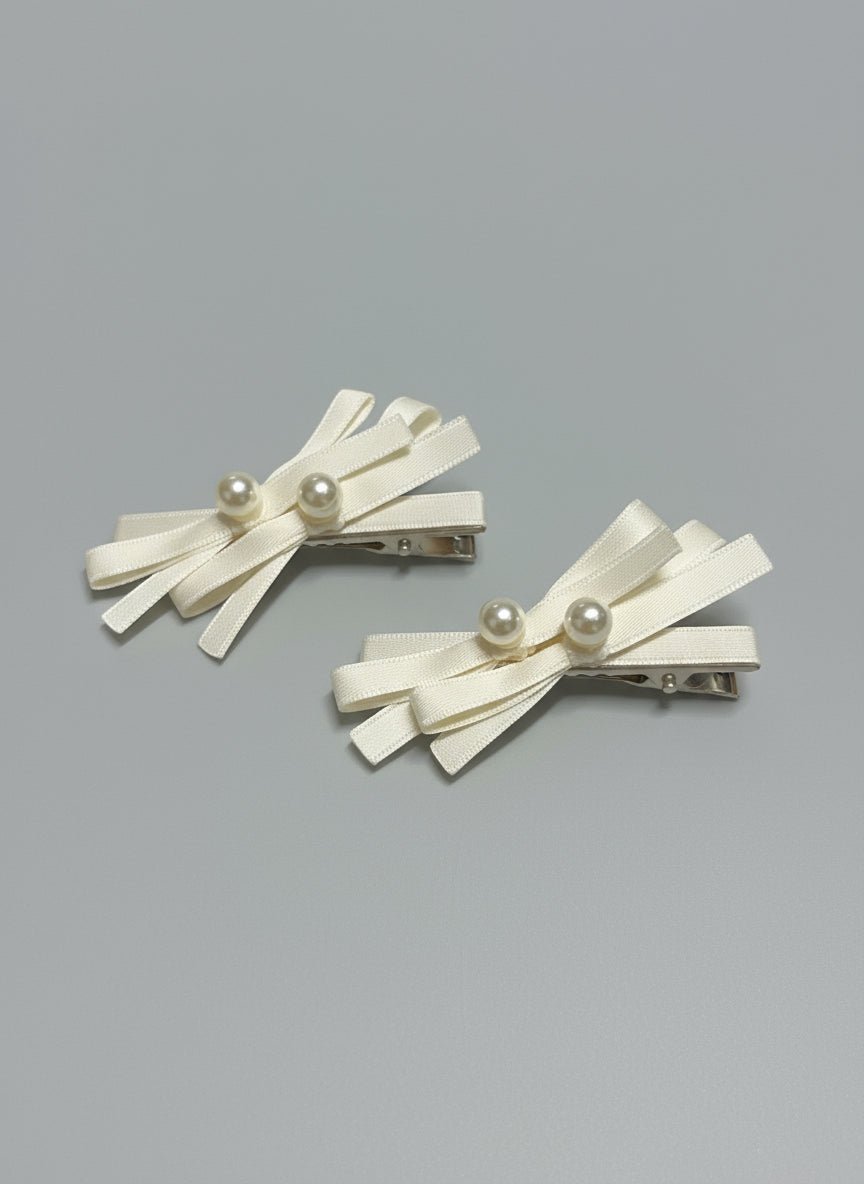 Pair of decorative hair clips with layered ribbons and pearls on a gray background