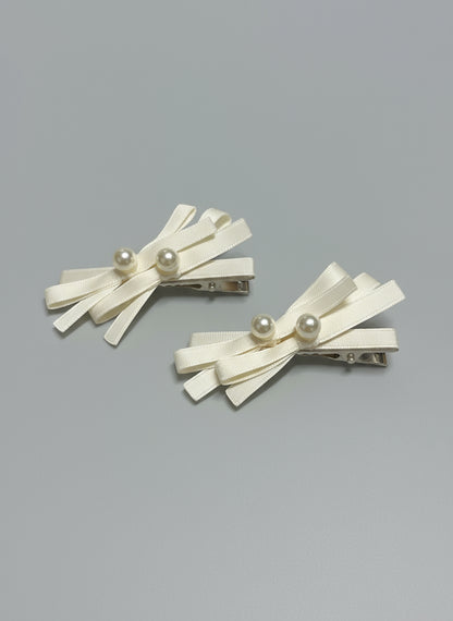 Pair of decorative hair clips with layered ribbons and pearls on a gray background