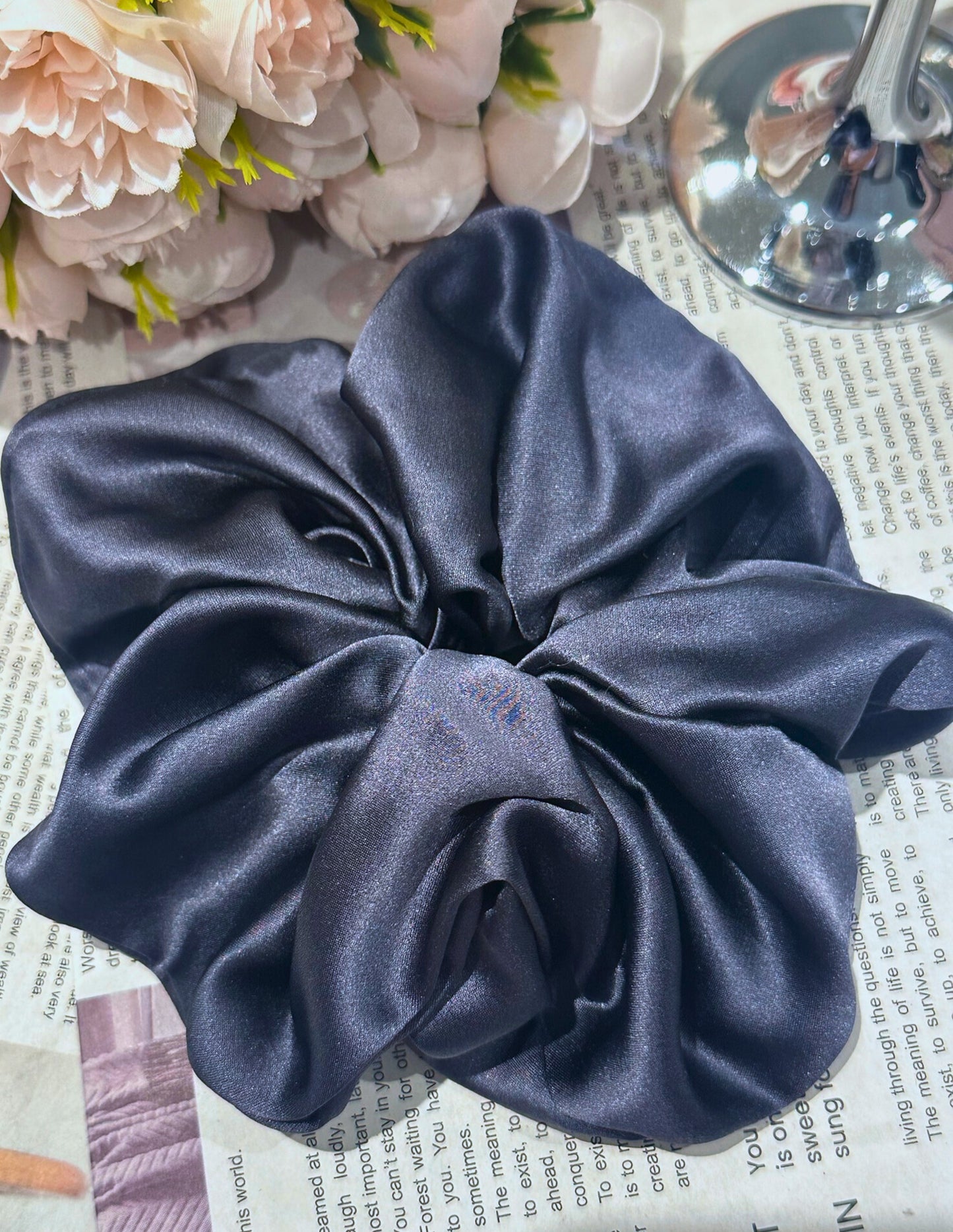 Navy handcrafted 30mm mulberry silk scrunchie on a newspaper background with flowers and a spoon.