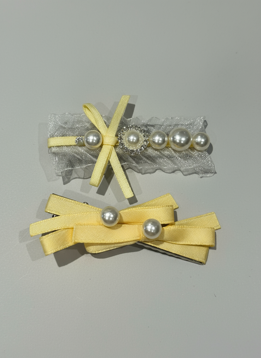 Two yellow hair bows with pearl embellishments on hair clips a gray background