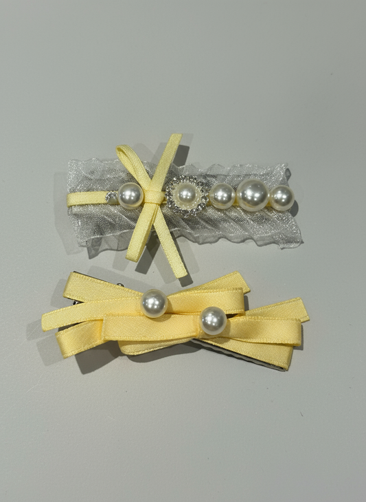 Two yellow hair bows with pearl embellishments on hair clips a gray background