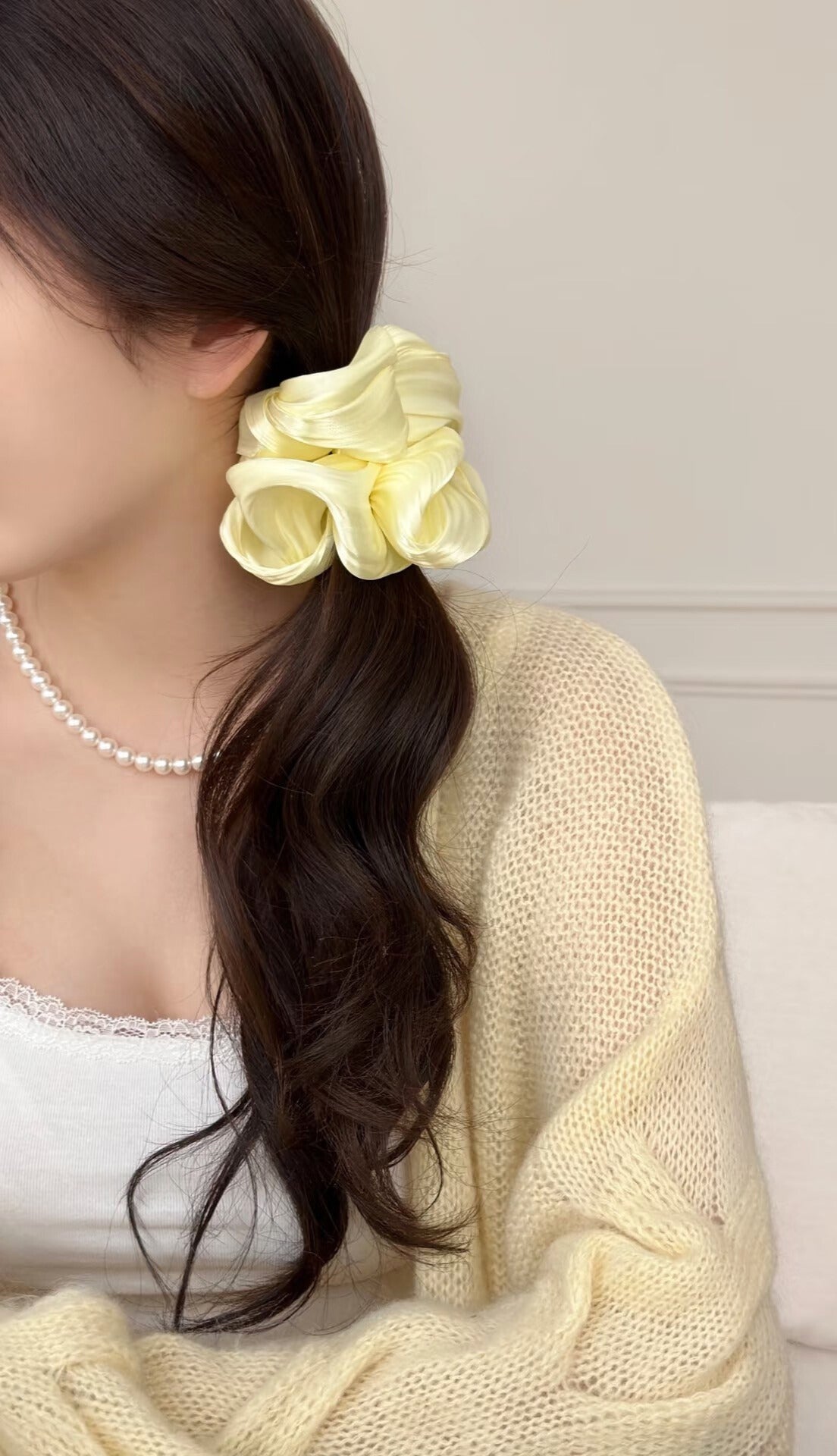 Woman with a yellow organza hair scrunchie in her hair, wearing a white top and beige cardigan. only at petite murmure