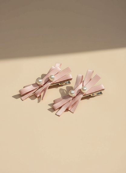 Two pink hair bows with layered bows and pearl centers on a beige background