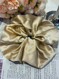 Beige handcrafted 30mm luminous mulberry silk scrunchie  on a newspaper background with flowers in the corner