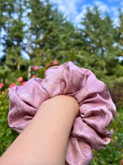Pink handmade rose aromatic scented mulberry silk scrunchie held by a hand with a blurred green outdoor background