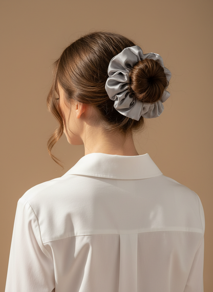 Woman with a bun holding a Silver Gray  handcrafted 30mm mulberry silk scrunchie against a beige background