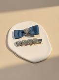 Blue bow hair clip with blue ribbons and heart shape Swarovski crystals on a beige surface