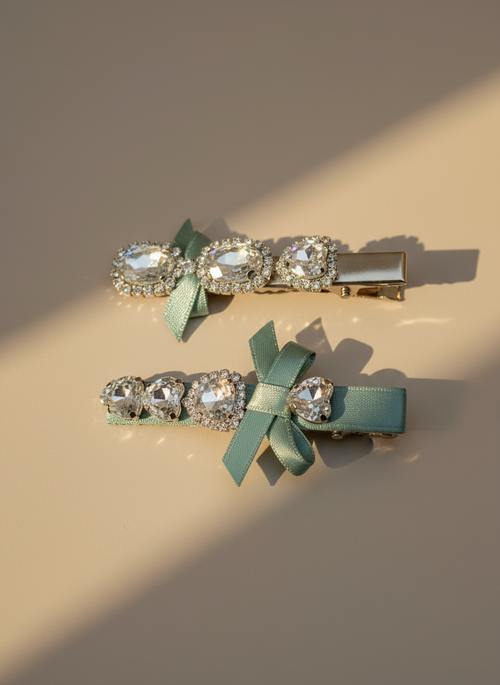 Two decorative hair clips with aqua-green ribbons and Swarovski crystals on a beige background.