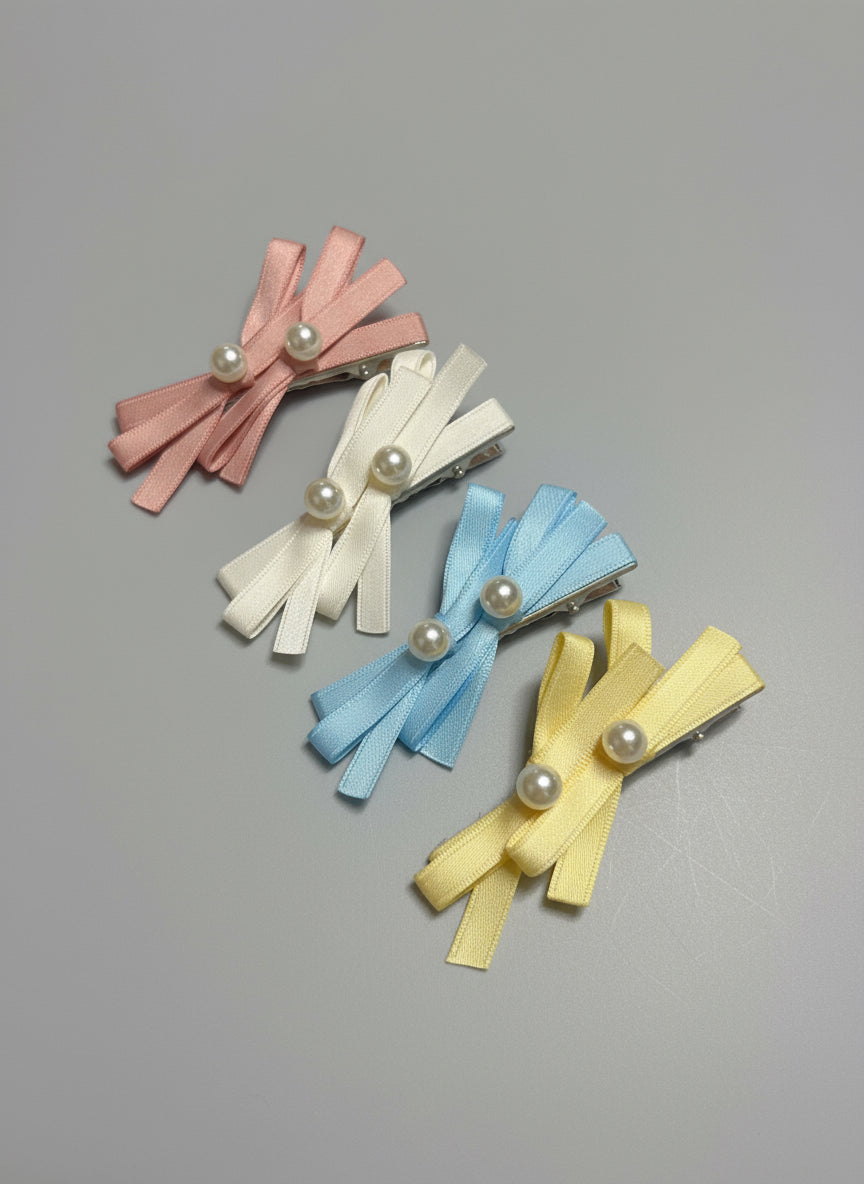 Four ribbon hair clips in pink, white, blue, and yellow with pearl centers on a gray background.