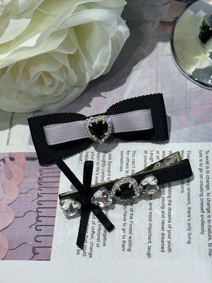 Two decorative hair bows with black ribbons and heart-shaped Swarovski crystals centers hair clips on a newspaper background.