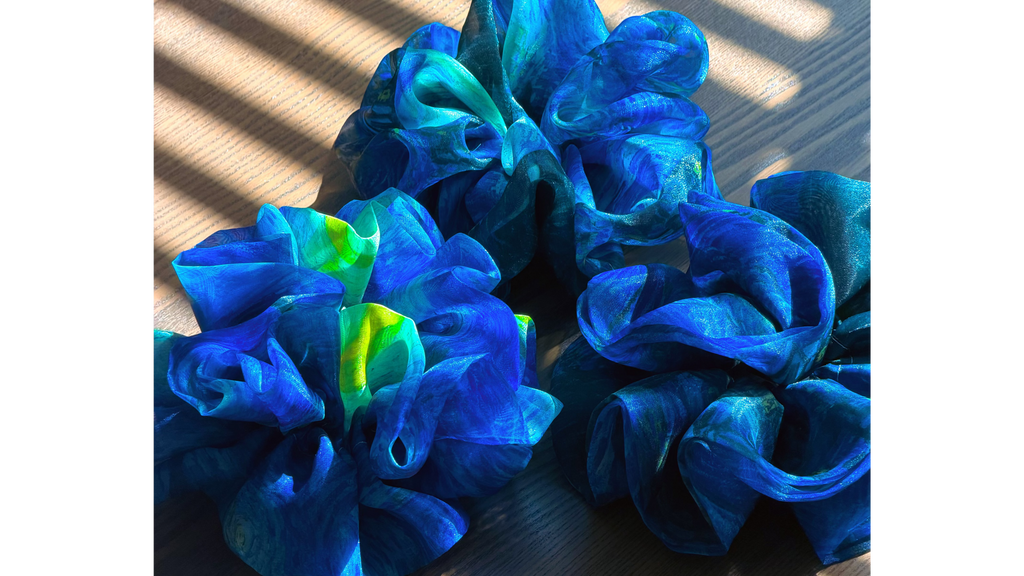 Three blue, green and yellow large organza scrunchies that inspired by Van Gogh's the Starry Night, only at Petite 
Murmure on a wooden surface with sunlight casting shadows