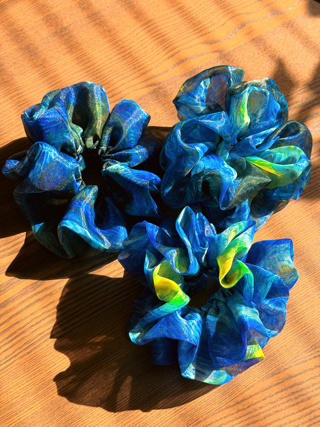 Three blue, green and yellow large organza scrunchies that inspired by Van Gogh's the Starry Night, only at Petite 
Murmure, scrunchies on a wooden surface