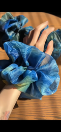 The blue, green and yellow large organza scrunchies that inspired by Van Gogh's the Starry Night, only at Petite 
Murmure on a wooden surface with a model's hand holding one of them display.