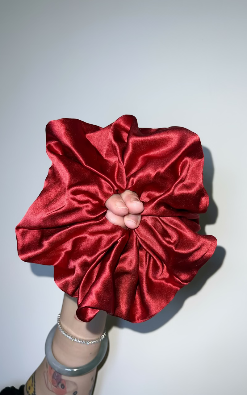Red handcrafted 30mm mulberry silk scrunchie held against a plain background