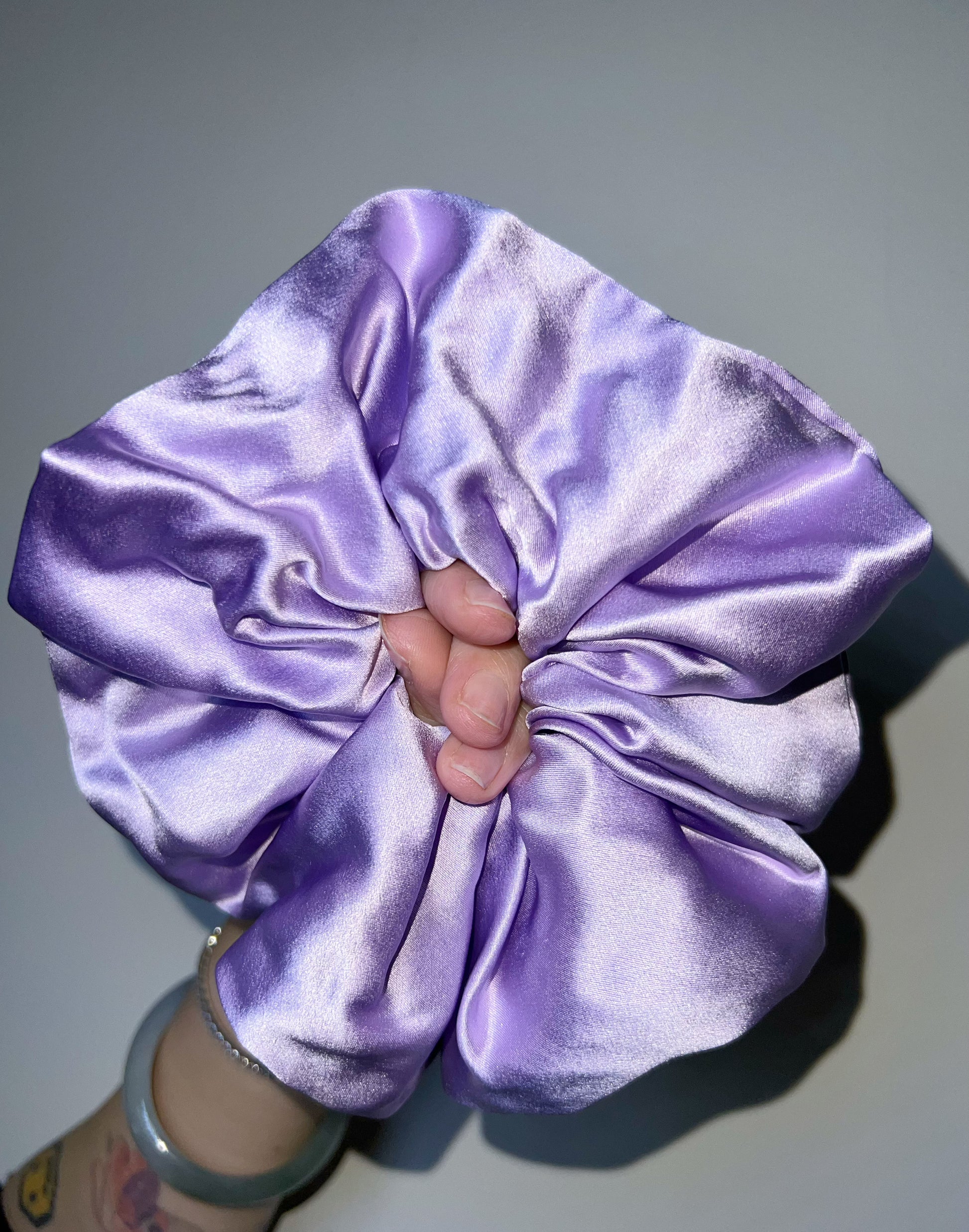 Lilac/ Lavender handcrafted 30mm mulberry silk scrunchie held by a hand against a gray background