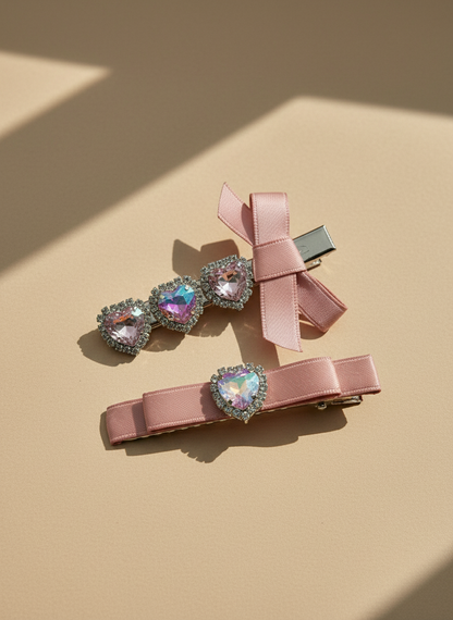 Two pink decorative hair clips with pink bows and heart shape Swarovski crystal  details on a beige background