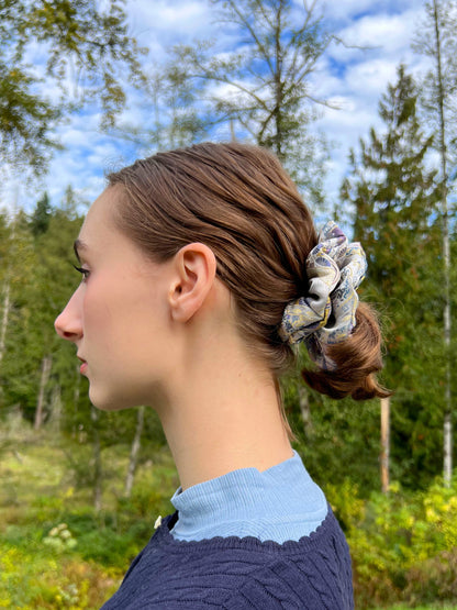 Woman with a Exclusive Song brocade mulberry silk scrunchie with peony aromatic scent, infused with gold thread. Phoenix patterned scrunchie in her hair standing in a forest