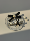 Set of hair accessories including a hair clip with black ribbons , Swarovski crystals and pearls on a reflective surface.