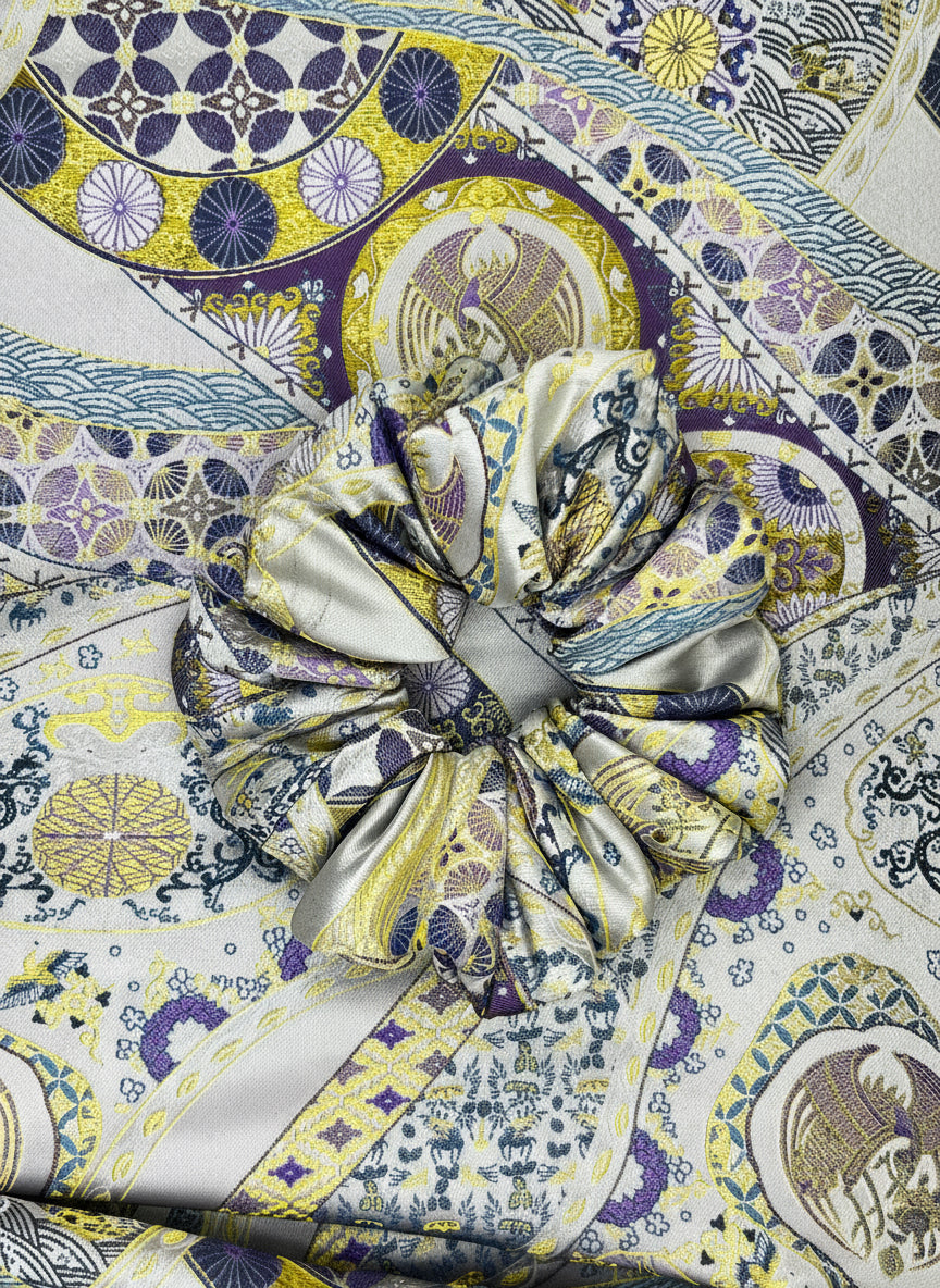 Close-up of a patterned fabric with a prominent Exclusive Song brocade mulberry silk scrunchie with peony aromatic scent, infused with gold thread. Phoenix patterned scrunchie