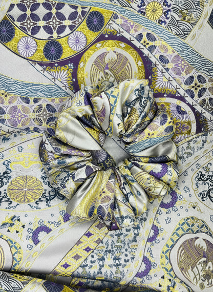 Close-up of a patterned fabric with a prominent Exclusive Song brocade mulberry silk scrunchie with peony aromatic scent, infused with gold thread. Phoenix patterned scrunchie