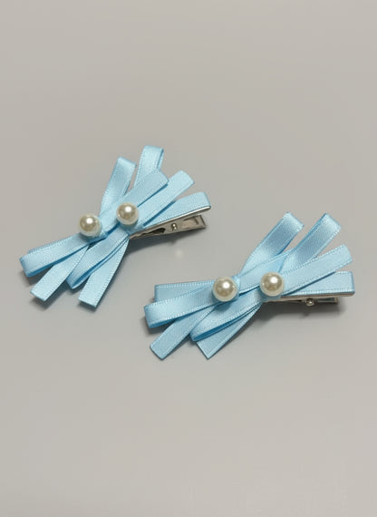 Two hair clips in light blue ribbon hair clips with pearl centers on a gray background
