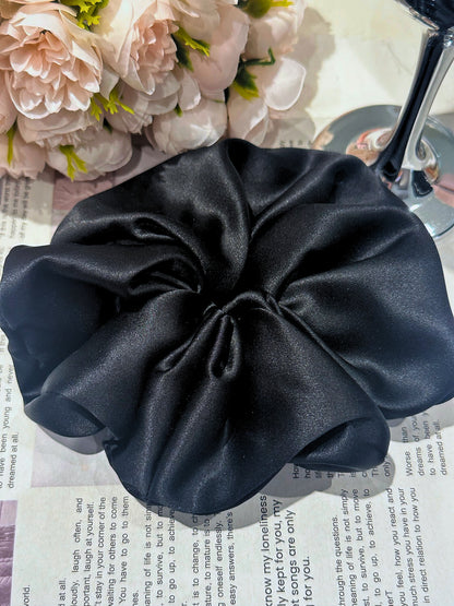 Black handcrafted 30mm mulberry silk scrunchie on a surface with flowers in the background