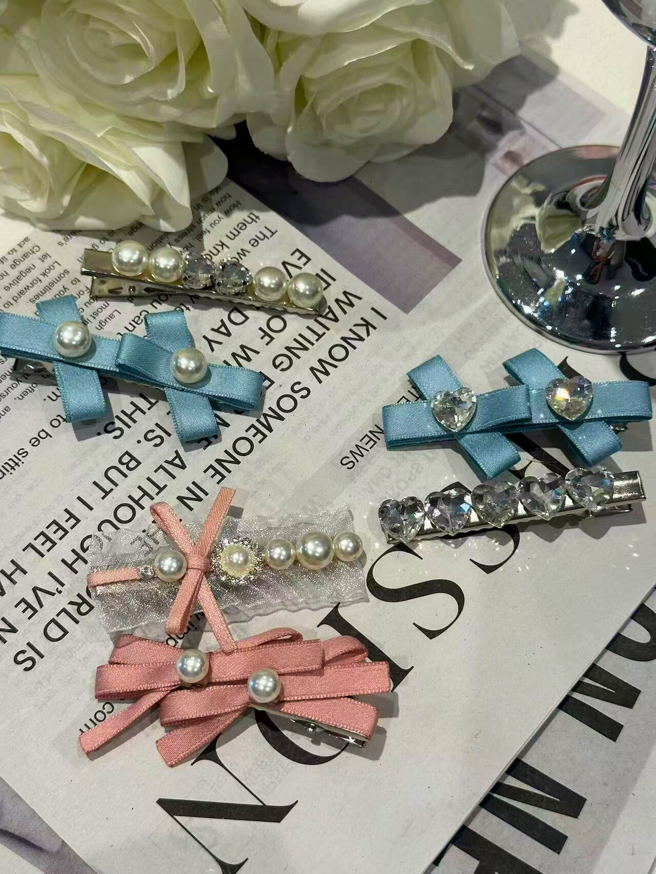 Set of decorative hair clips with embellishments, such as pearls, organza, ribbons and Swarovski crystals elements on a newspaper background