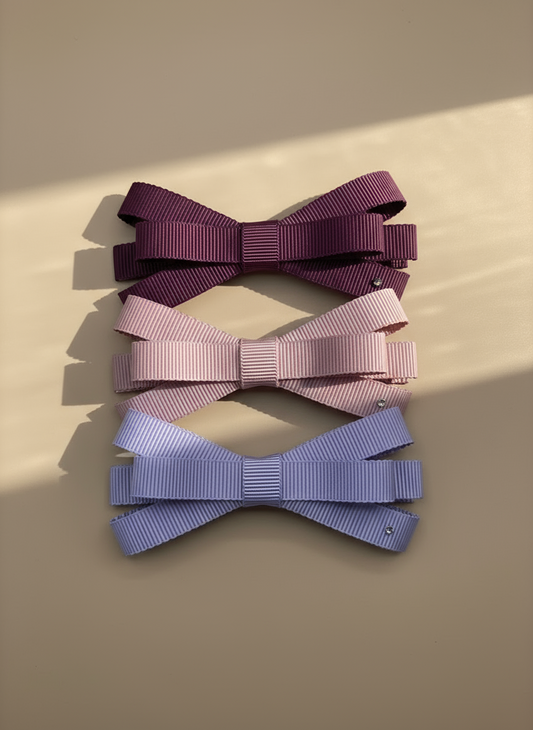 Three ribbed hair bows in purple, pink, and blue with tiny rhinestone on a beige background