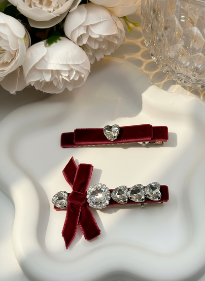 Two red hair clips with Swarovski crystals  details on a white surface with flowers in the background